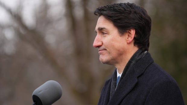 Prime Minister Justin Trudeau speaks into a microphone while wearing a long, blue coat