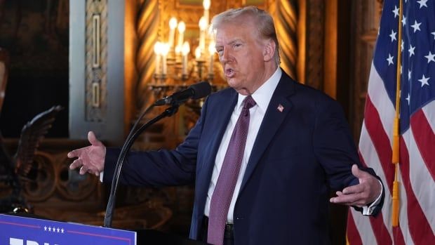 Donald Trump gestures from behind a podium that says 'Trump Vance'