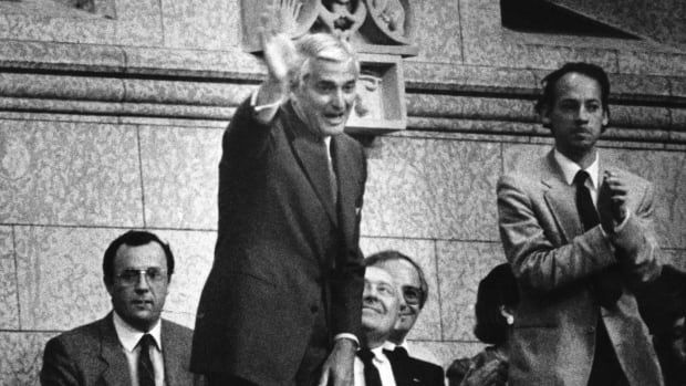 A man stands and waves as others applaud.