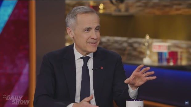 Former Bank of Canada and Bank of England governor Mark Carney speaks to The Daily Show host Jon Stewart during an appearance. The image is of Carney smiling as he speaks to Stewart who is off camera. 