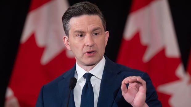 A still of a man in a suit speaking in front of two Canadian flags