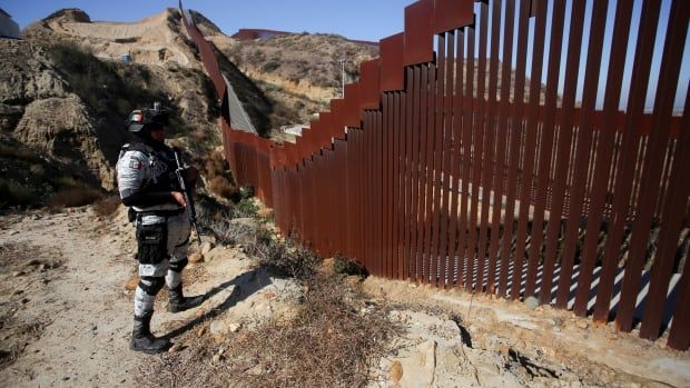 A soldier stands near a border fence.