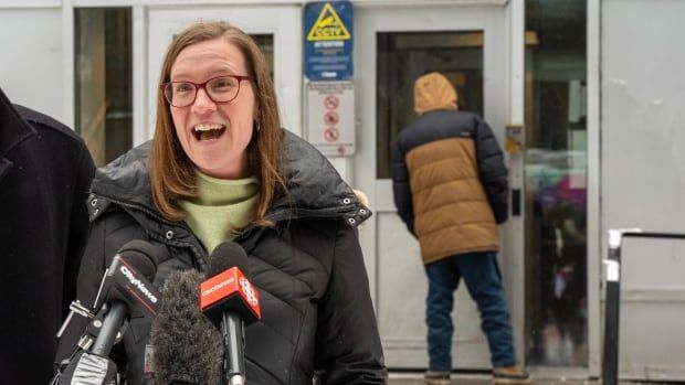 A woman speaks into microphones outdoors in winter.