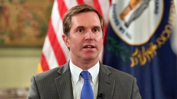 Andy Beshear speaks while wearing a grey suit and blue tie