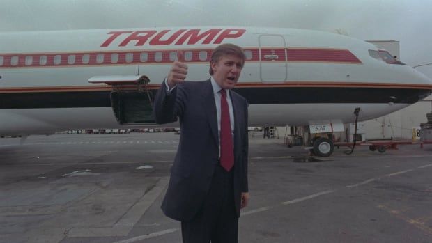 A person gives a thumbs-up gesture in front of an airplane that has the word "TRUMP" painted on the side. 