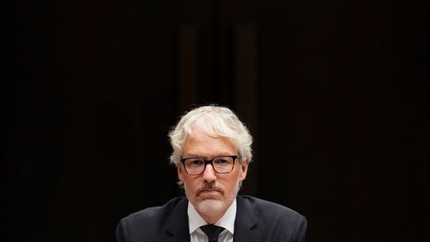 A government official listens at a meeting. The background is all black.