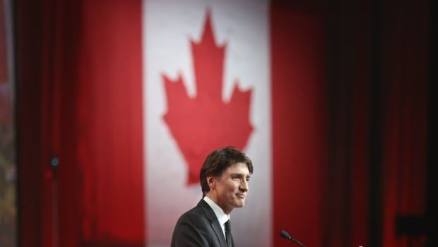 A person speaks in front of a large Canadian flag.