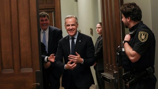 A man in a suit smiles as he walks through a large wooden door.