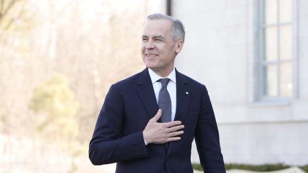 A grey-haired man in a suit and tie walks into a stone building.