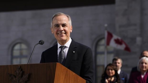 A grey-haired man in a suit smiles at a podium.