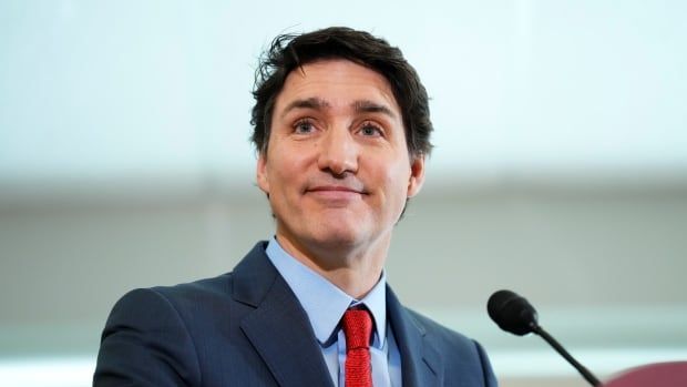 A man in a blue suit with a red tie stands in front of a podium.