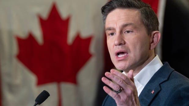 A man in a blue suit stands in front of a Canadian flag.