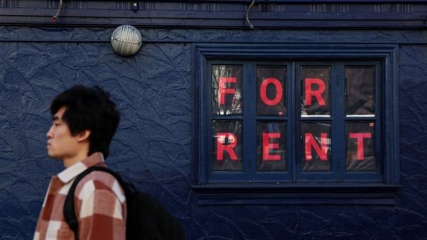 A man in a plaid jacket walks by a for rent sign.