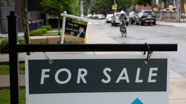 For sale signs hanf in front of houses on a street wet from rain, with a cyclist appoaching.