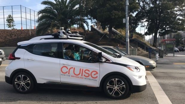 A white car with the word "Cruise" on the side is seen at a side angle in a parking lot. 