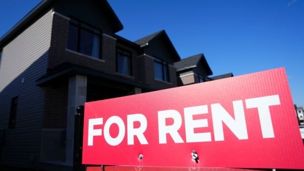 A upwards angle shows a bright red "FOR RENT" sign with a house beyond it and the blue sky past them all. 