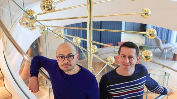 Two men stand on a staircase at the offices of Google DeepMind UK with a brass sculpture of balls on sticks behind them.