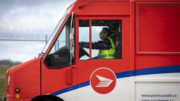 A postal worker is pictured in the driver's seat of a delivery truck.