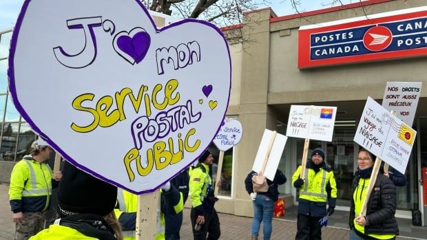 A scene outside a postal office where workers are striking. A heart-shaped sign reads "I love my public postal service' in French.