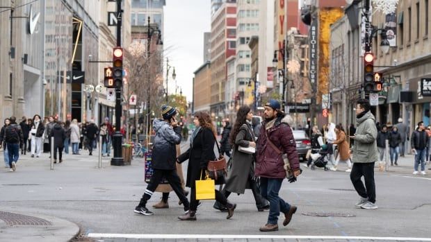 People cross the road on a city street. Most are wearing coats. 