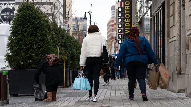 Shoppers carrying bags walk down a sidewalk.