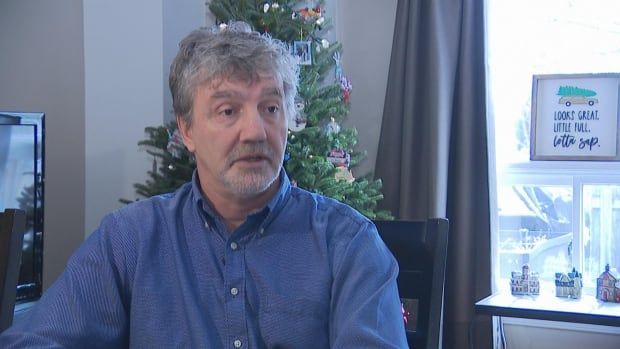 A man wearing a blue button-up shirt sits in front of a christmas tree.