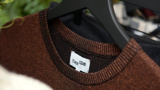 A brown sweater is shown on a hanger with its brand label on display.