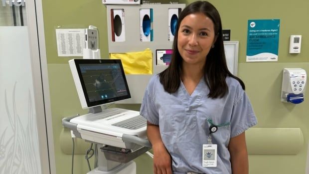 Healthcare worker in a hospital setting wearing scrubs looking at camera, standing beside health equipment. 