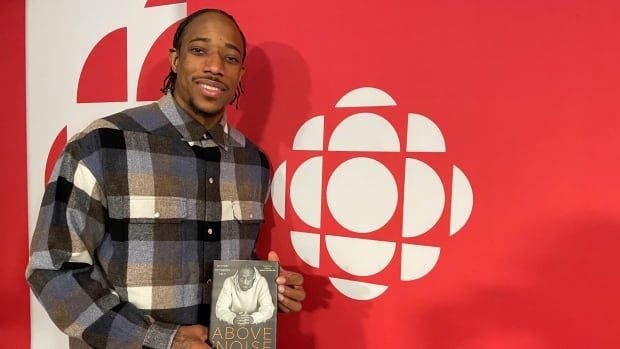 A man holds a book in front of a CBC logo.