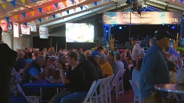 People sitting at long tables under a huge tent at shellfish festival.