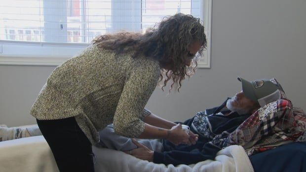 Photo of a woman tending to a man in a bed. 