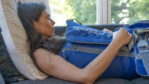 A woman is lying on a couch with her eyes closed. She is wearing a blue inflatable suit that is zipped up on the side.