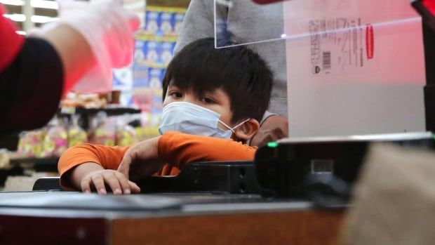 A young boy wearing a mask during a transaction with a cashier in 2020.