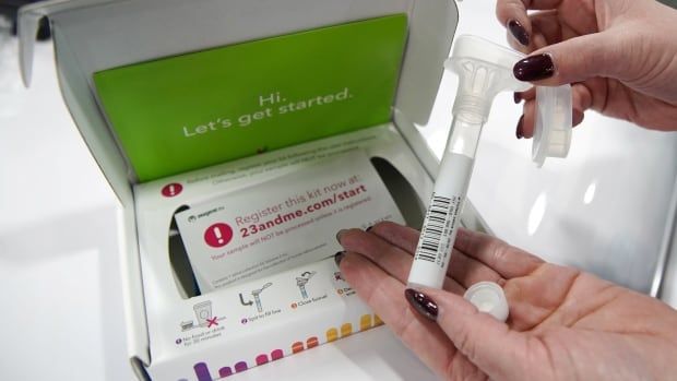 A person holds up part of a DNA testing kit provided by 23andMe.