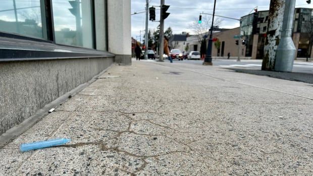 A plastic, blue piece of drug paraphernalia lays next to a building with cars and people in the background