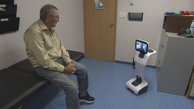 A man sitting on a therapy bed and a standing robot