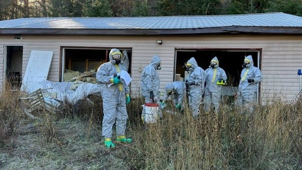 A group of people in hazmat suits outside a rundown property.