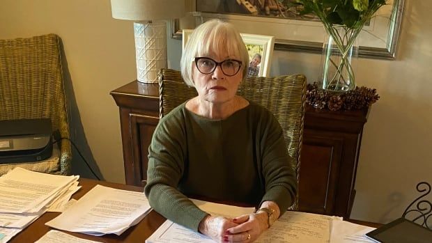 Woman sits at table with stacks of paper around her