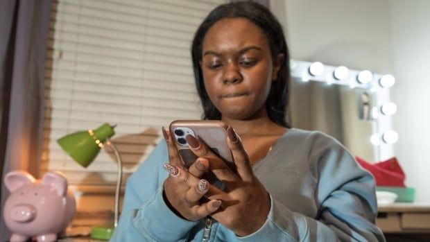 A teen girl wearing a blue hoodie is looking at her cellphone. 