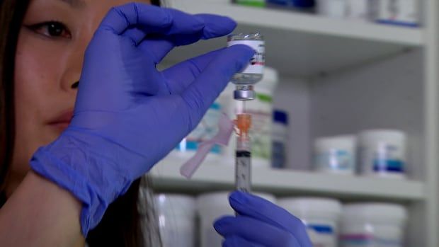 A woman fills a syringe from a vial. 