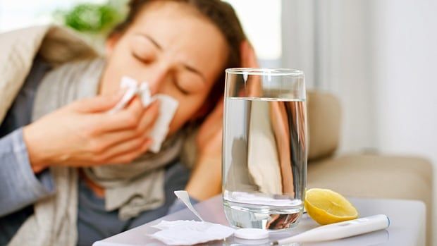 A woman lies in bed blowing her nose.