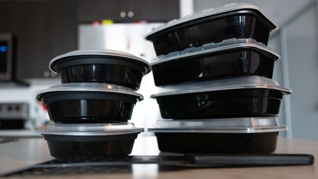 A stack of black plastic takeout containers with a black plastic spatula in the foreground.