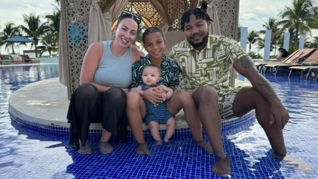 A woman, two boys, and a man sit in splash pool at a tropical resort.