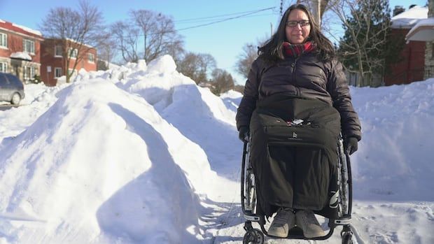 Female wheelchair user poses beside a large snow bank in Montreal.