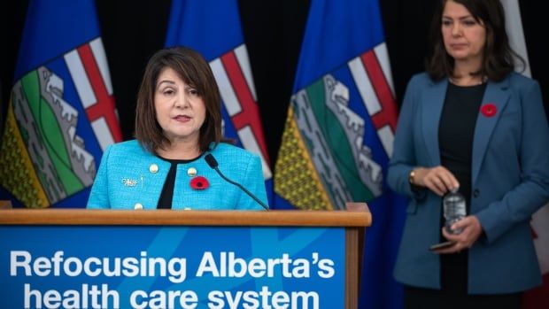 A woman address the media from behind a podium as another woman looks on.