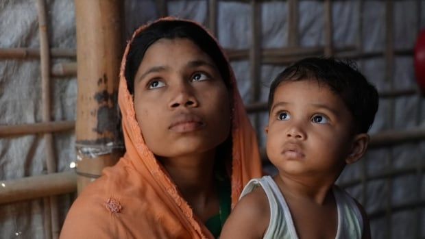 A woman with an orange head scarf holding her daughter looks up off camera.