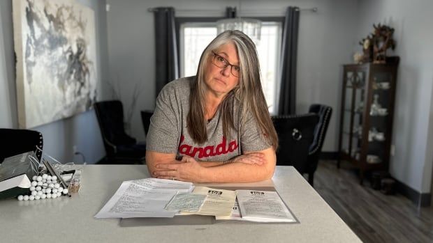 A woman leans over a kitchen countertop and stares into the camera with a sad expression.