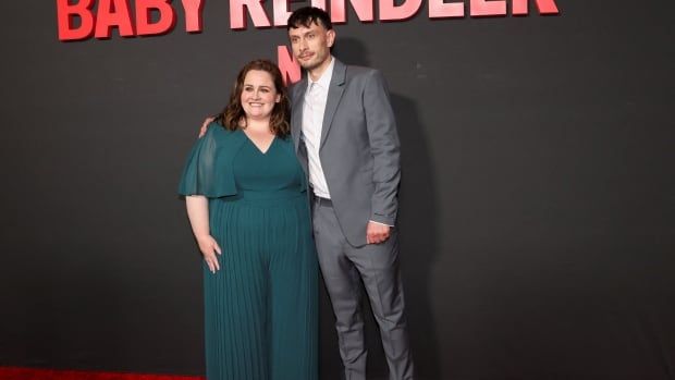 A man and a woman stand on a red carpet. 