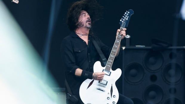 A man plays a white electric guitar on stage. 