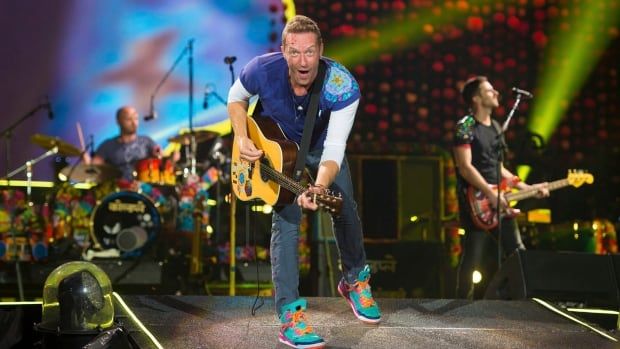 Lead singer of Coldplay Chris Martin plays guitar at a concert on stage.